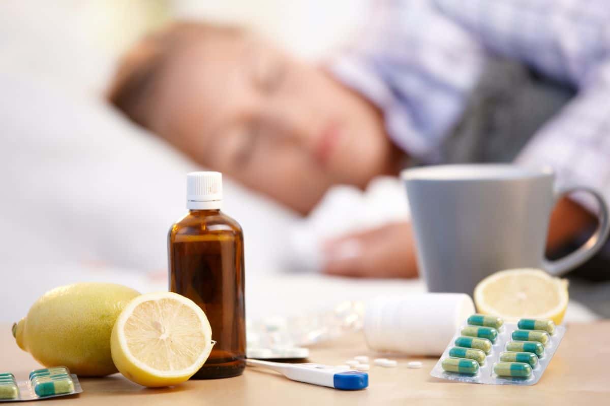 Medicine, thermometer, and tea with a woman asleep in the background